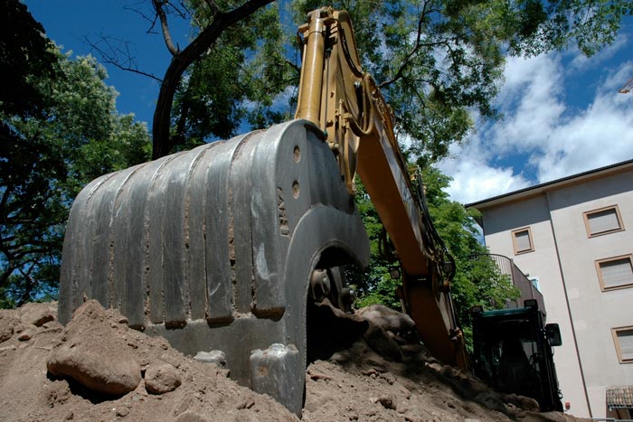 En gul grävmaskin utför markarbeten vid en byggarbetsplats under sommaren